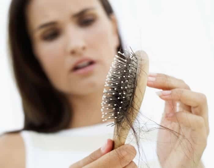 Blurred image of a woman looking and holding up a hairbrush with a giant wad of hair (hair loss image).