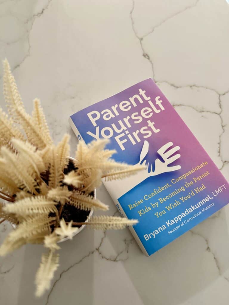 flatlay image of the book "Parent Yourself First" next to a tan faux plant on a counter.