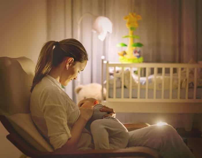 woman sitting in chair inside of nursery room feeding baby a bottle of milk