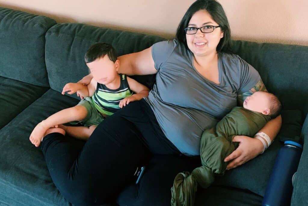 image of karissa of Mom After Baby sitting down holding her newborn and her young toddler.