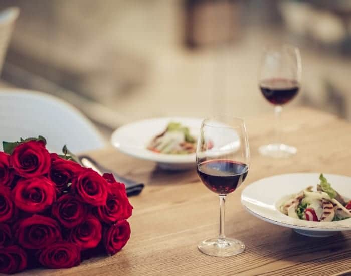 close up shot of a romantic meal and table spread with a glass of wine, roses, and grilled chicken