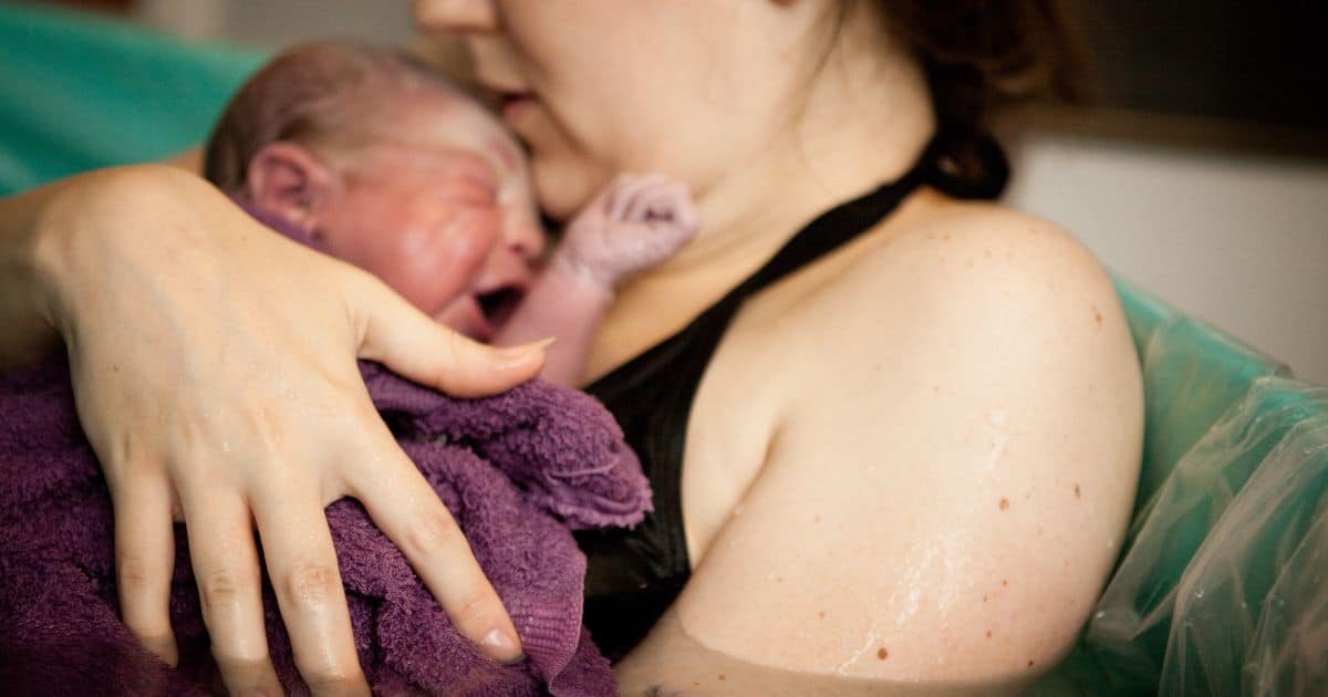 close up image of a newborn being hugged by it's mother after birth in a water tub