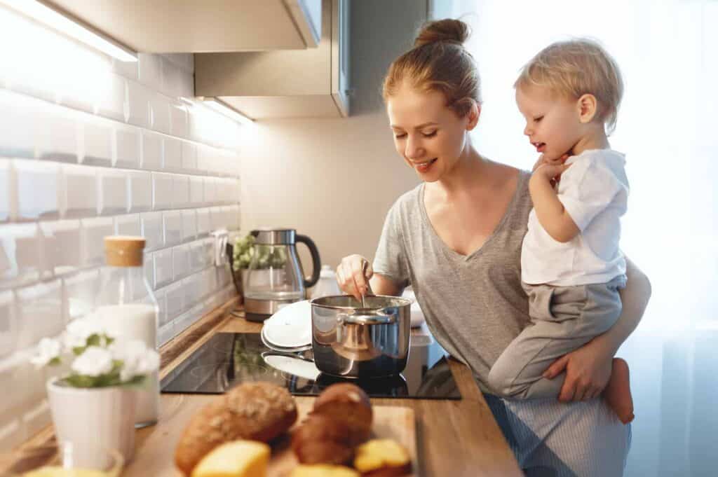 Mom holding little boy while mixing food on the stove