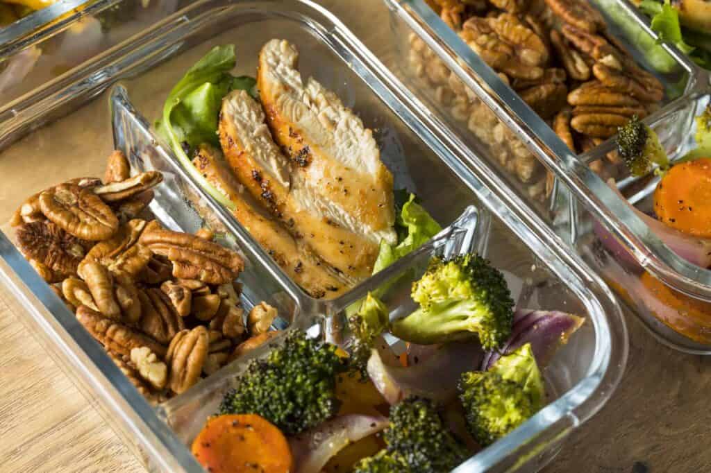 Image shows glass container with chicken breast, roasted vegetable blend, and pecans inside. 