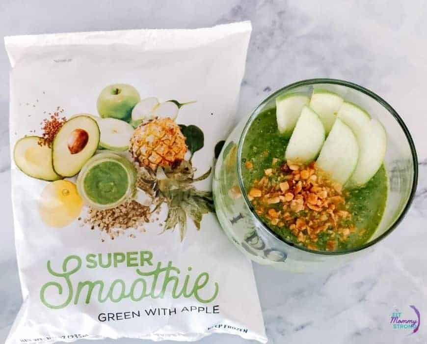 image shows a smoothie bag next to a glass with a green smoothie inside topped with granola and apples