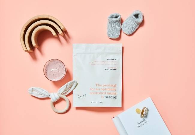 needed prenatal vitamins displayed in a flatlay design next to baby socks, a baby teether and wooden rainbow — breastfeeding basket essential item
