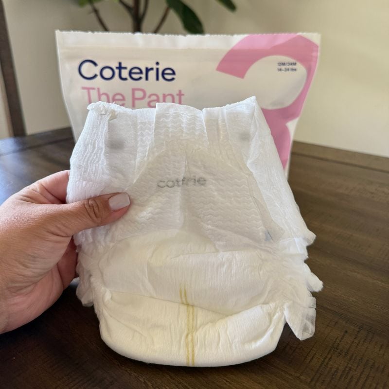 close up image of my hand holding the Coterie baby Diaper (the pant design) with the packaging in the background