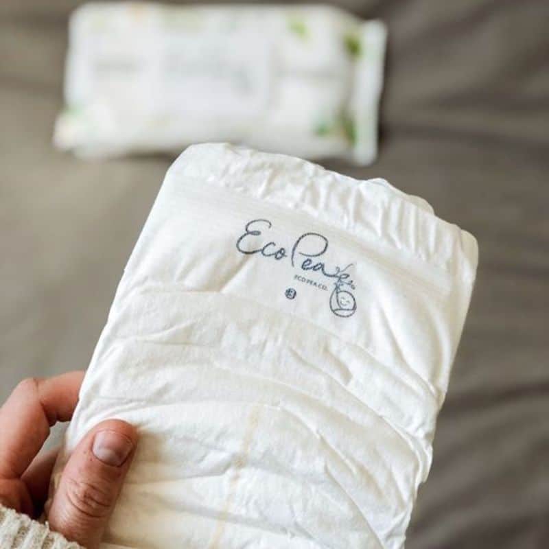 lifestyle close up image of hand holding up an Eco Pea Co.diaper with their wipes blurred in the background