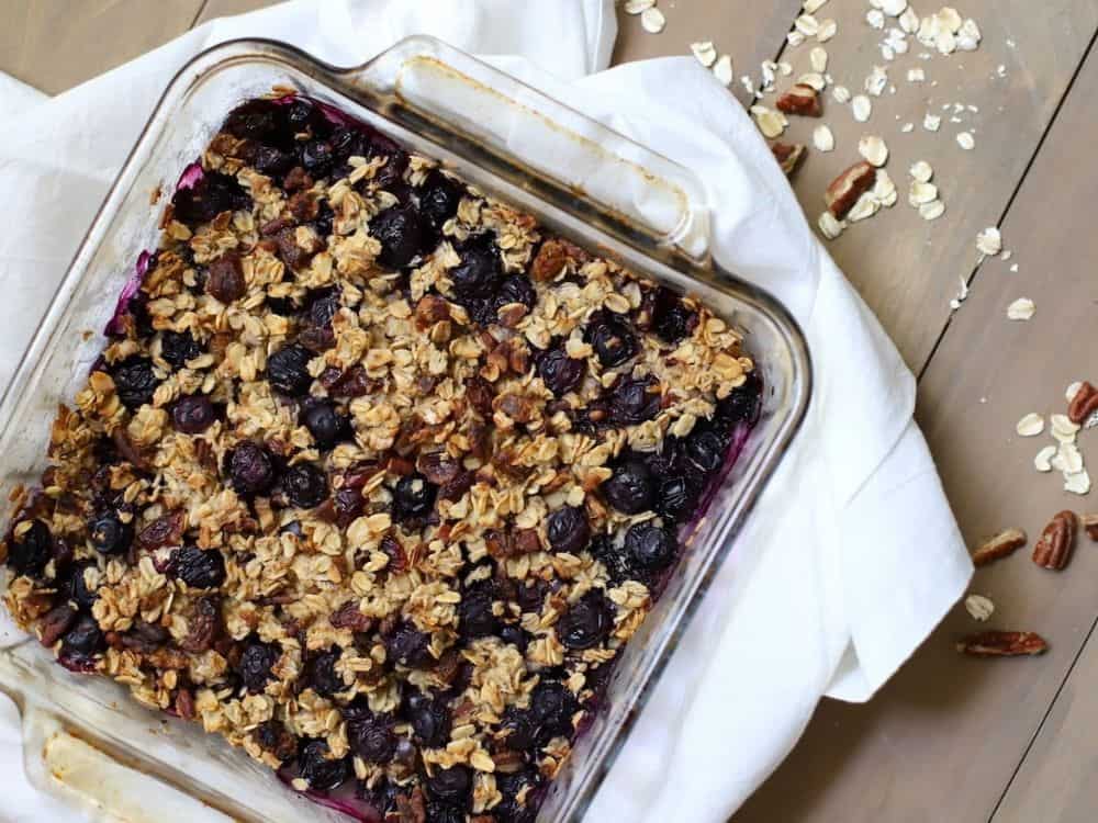 image shows a flatlay image of baked oatmeal in a glass dish with blueberries on top. 