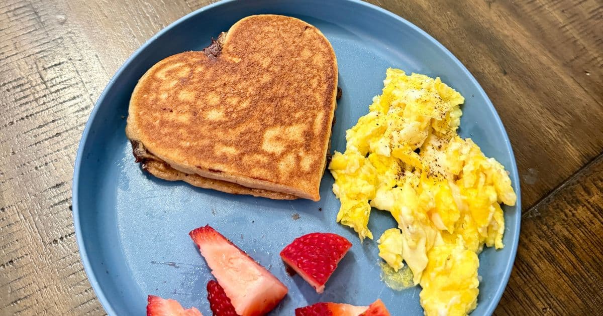 heart shaped pancake with scrambled eggs and strawberries on a blue plate