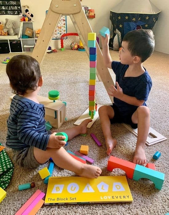 Two young toddler stacking colorful wood blocks from the Lovevery Montessori Subscription Box Play Kit