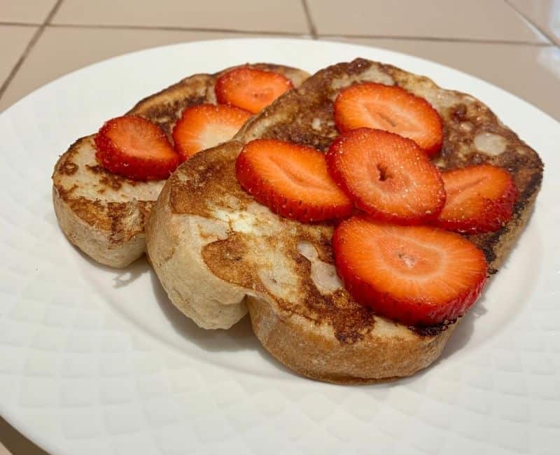Photo of french toast with strawberries on top all on a white plate