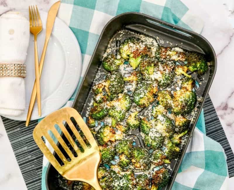 air fried broccoli recipe inside of air fryer, placed on a green checkered table cloth next to a gold spatula