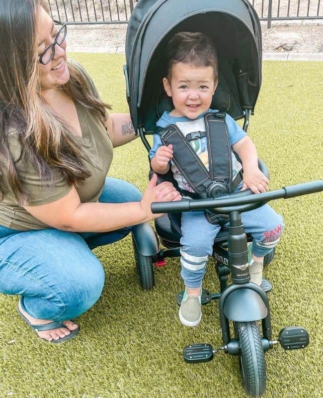 picture of me (karissa in a green shirt and blue jeans) looking at my son while he sits in his bentley stroller trike