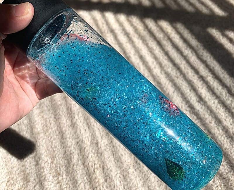 This image shows the completed glitter glue calming bottle being held under the sunlight to illuminate all of the sparkly glitter