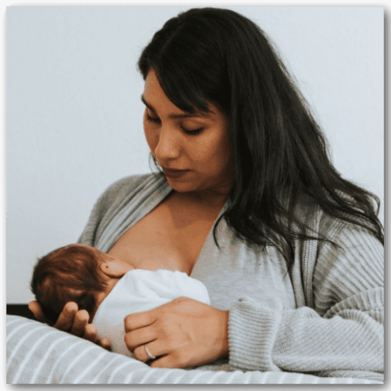 woman with dark hair breastfeeding infant baby in swaddle