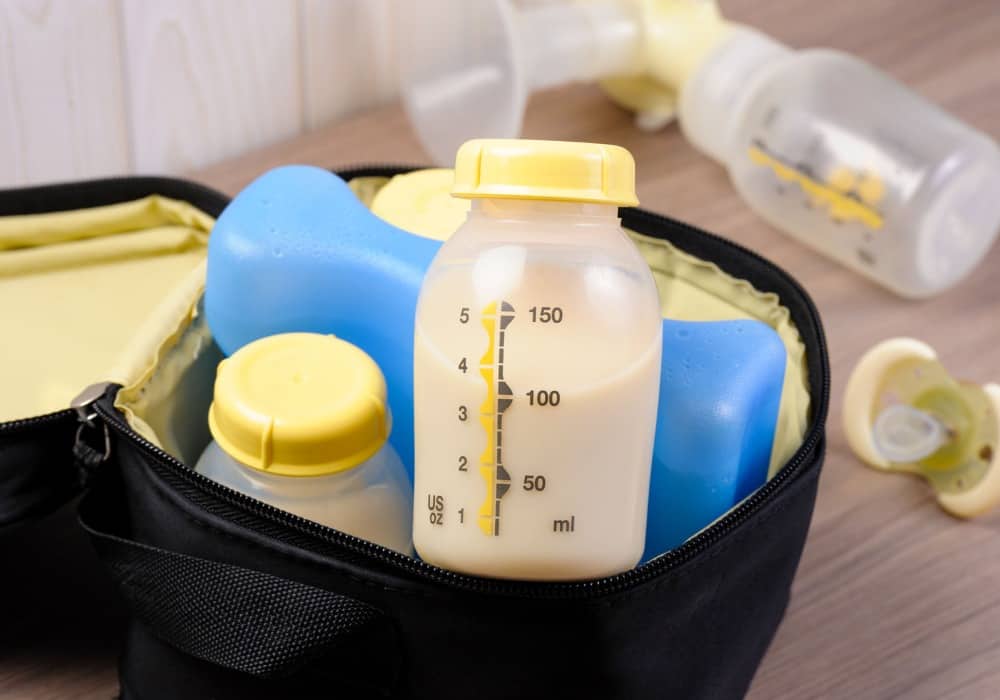 image shows close up photo of medela bottle with milk inside of a breast milk cooler bag and blue ice pack