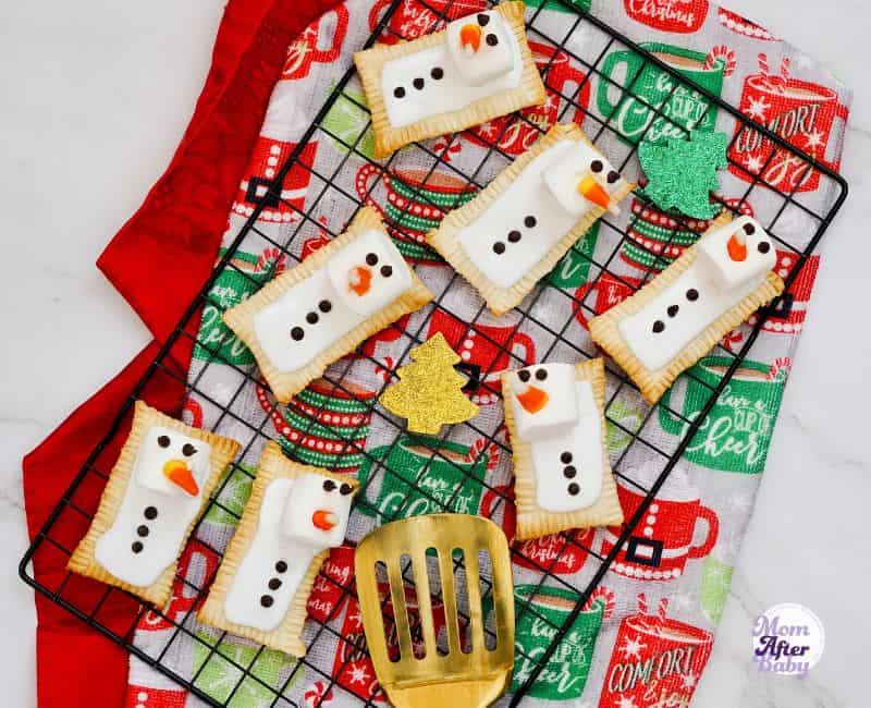 Snowman air fryer pop tarts set in a flat lay style on top of a cooling rack, on top of festive holiday towels in red and green colors.