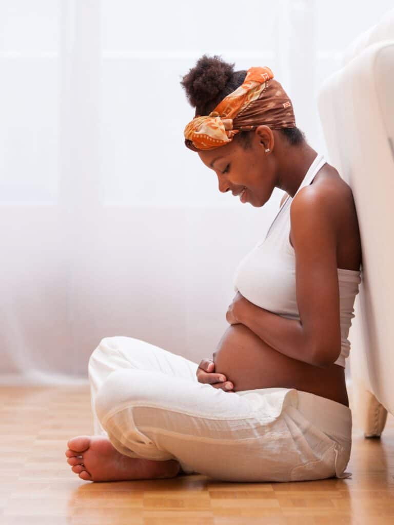 pregnant african american woman sitting on the floor, looking down and holding her pregnancy belly