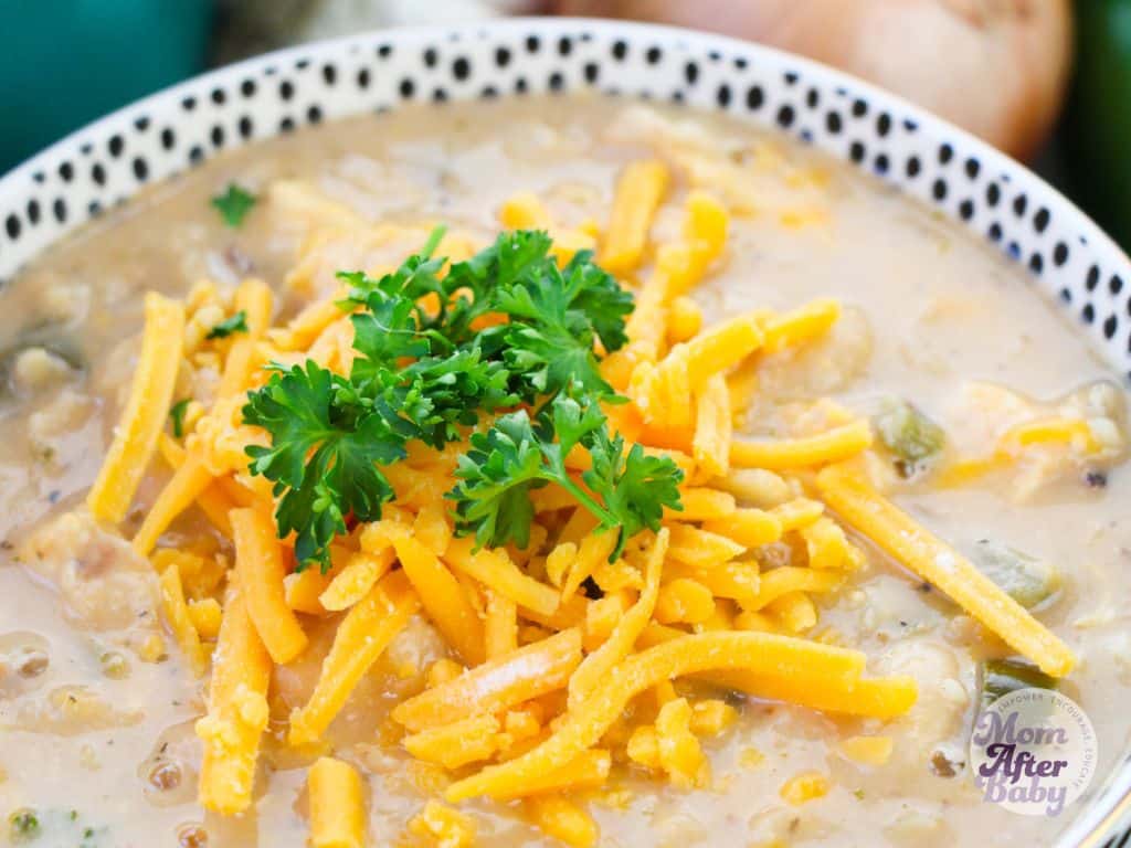 Close up photo of white chicken chili in a serving bowl topped with cheddar cheese and cilantro