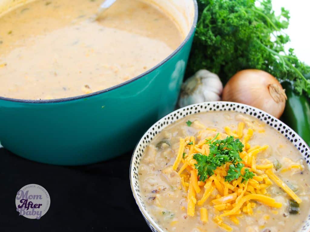 White chicken chili recipe with a small bowl of the recipe topped with cheddar cheese and cilantro in front of a large 6 quart teal dutch oven