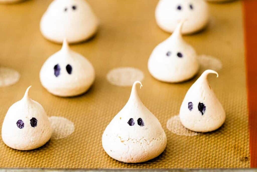 this image shows a bunch of white meringue ghosts on a tray for halloween