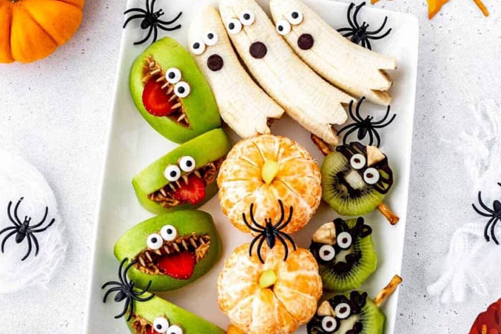 This image shows a fruit tray spread on a halloween themed countertop with halloween decorated fruits