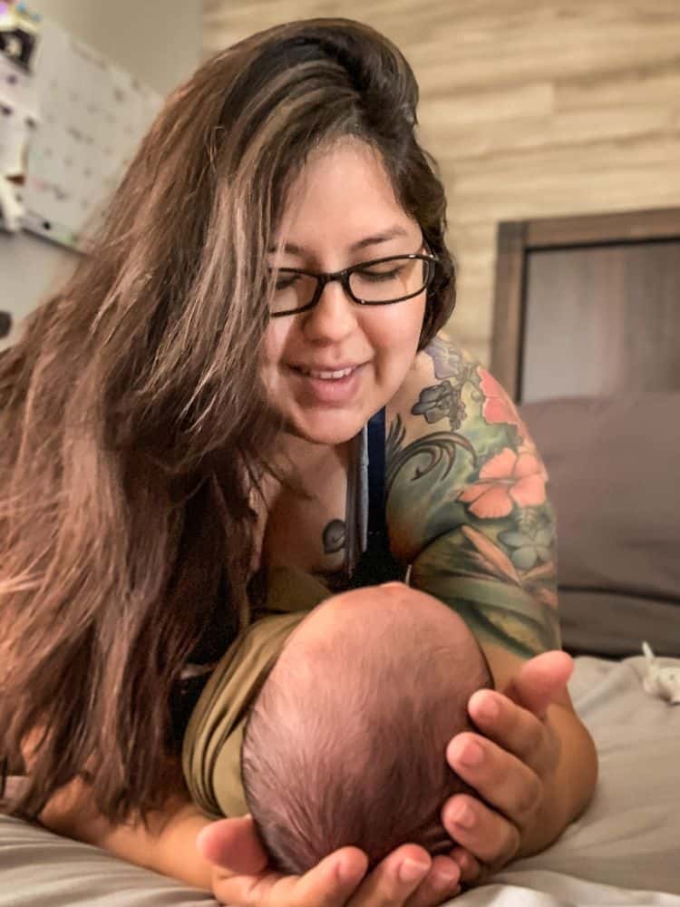 this image shows myself (a mom with long dark brown hair and glasses) looking down and smiling at my newborn baby who is looking up at me