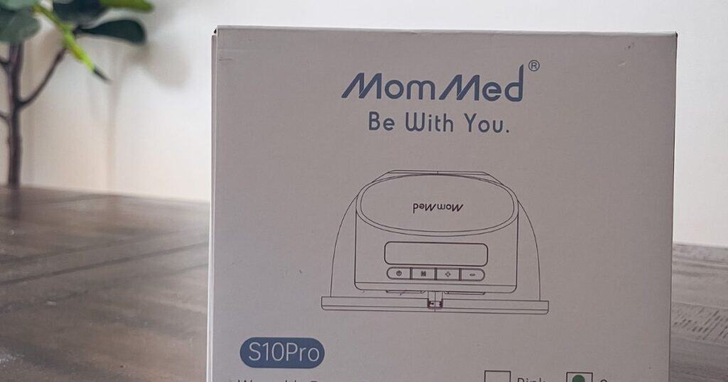 This blog cover image shows the S10 Pro Breast Pump Box on a table, the box says "MomMed, Be With You" and below is a purple stripe graphic with text that reads "S10 Pro Mom Med Breast Pump Review"
