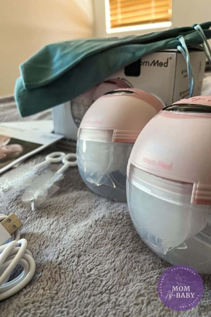 This image shows a close up side angle of the MomMed S21 breast pump in pink next to all of the items and accessories that come in the box