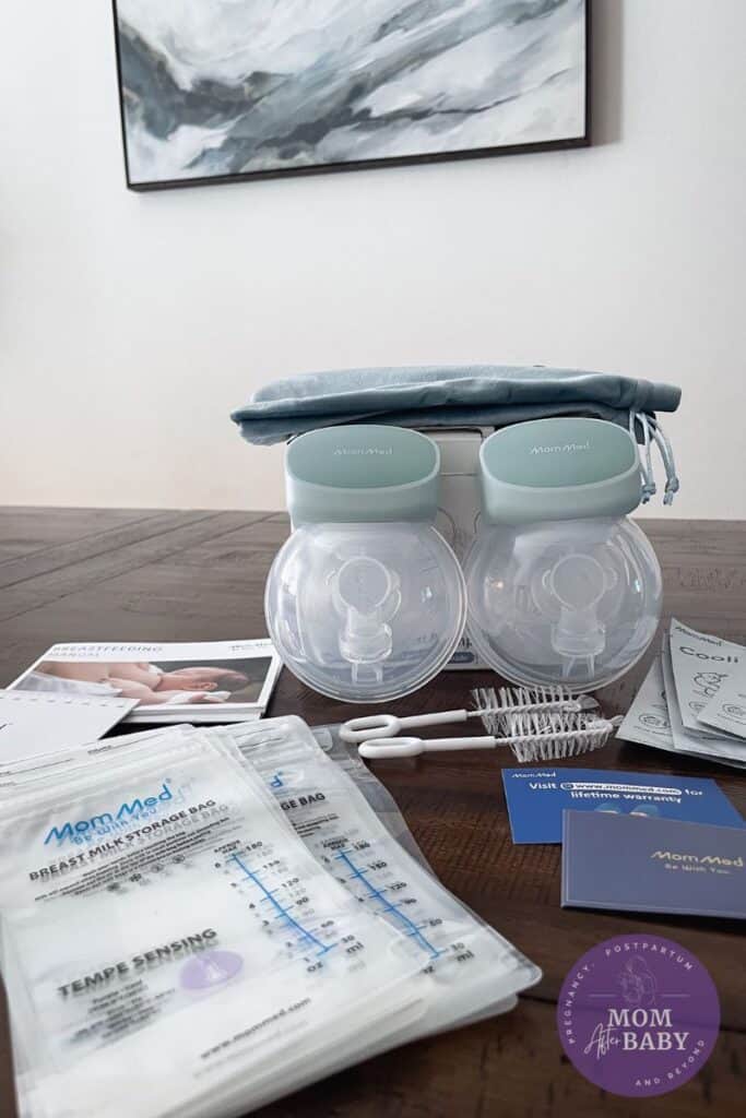 This image shows the MomMed S10 Pro box on a brown table along with all of the contents of the package unpacked on the table next to his. There are breast milk bags, accessories, breast pumps, and a marble looking photo in the background. 