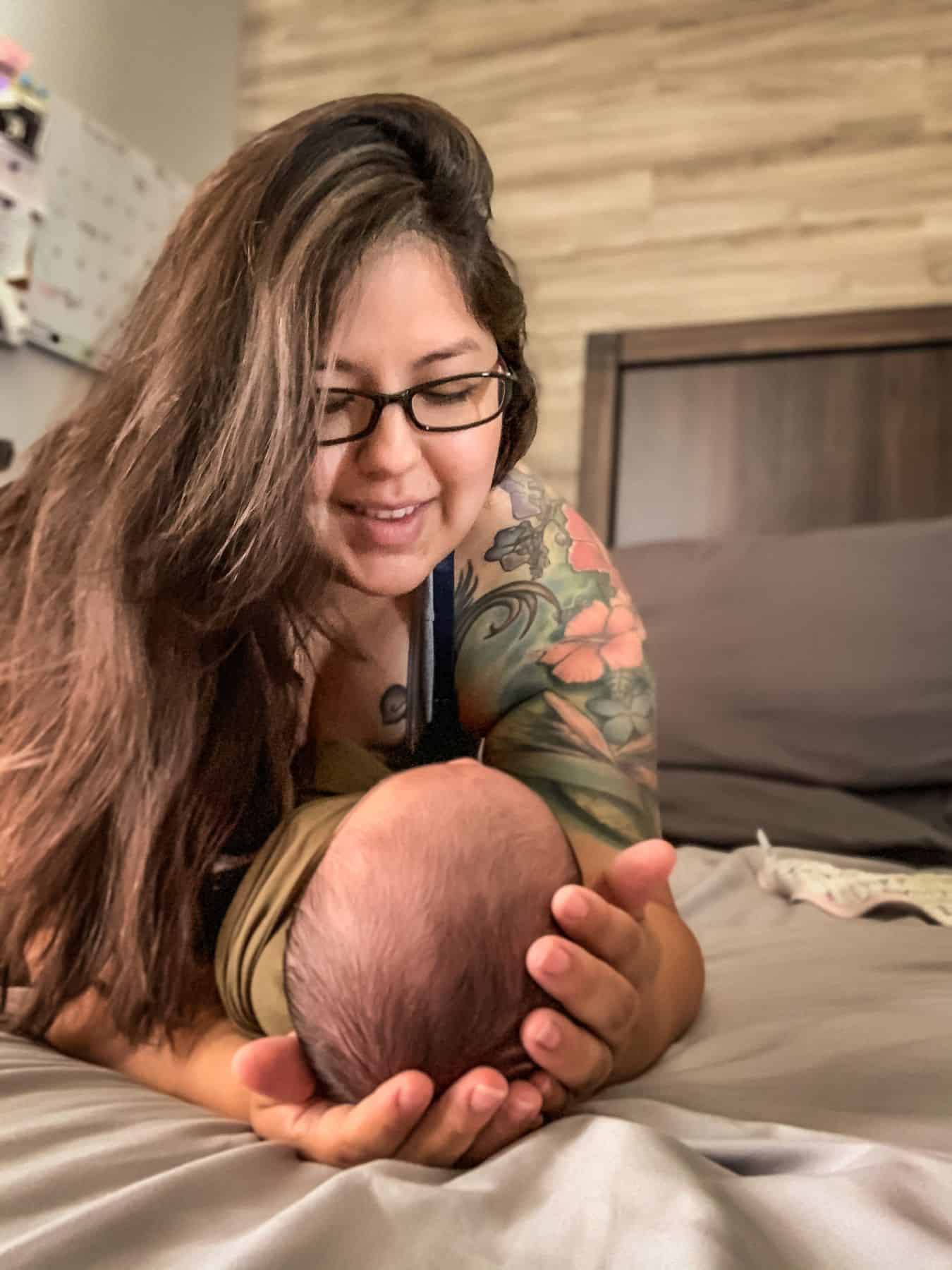 this image shows myself (a mom with long dark brown hair and glasses) looking down and smiling at my newborn baby who is looking up at me