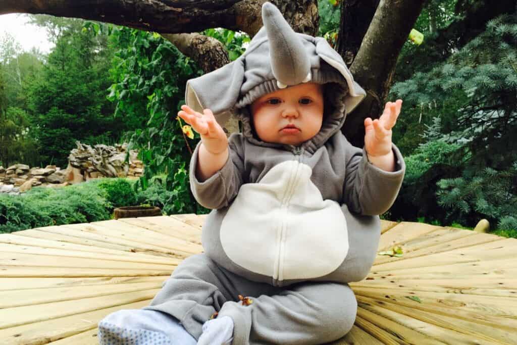 image shows an older baby sitting on the floor outside wearing a puffy elephant costume