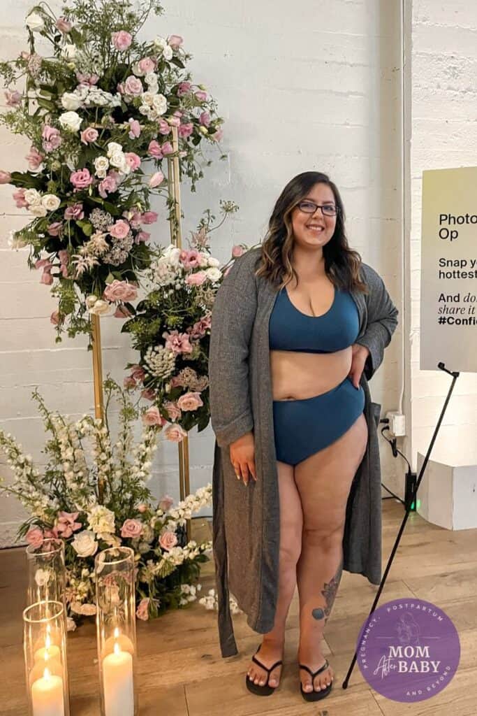 image shows myself, a brown haired woman in a blue knix bra and high-waisted underwear, posing and smiling at the Knix Confidence Tour. Background boho floral decor.