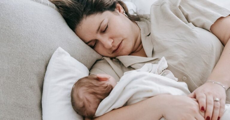 image shows a tired new mom snuggling her newborn baby while sleeping