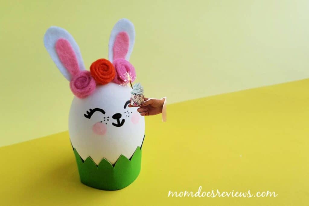 Picture of an adorable easter egg decorated as a bunny against a yellow backdrop. Made by Mom Does Reviews