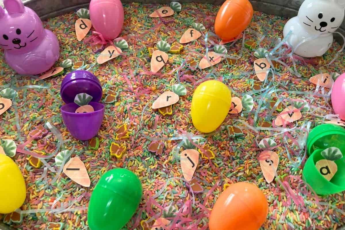 close up image of an easter sensory bin with plastic easter eggs, easter colored rice, letters, and more