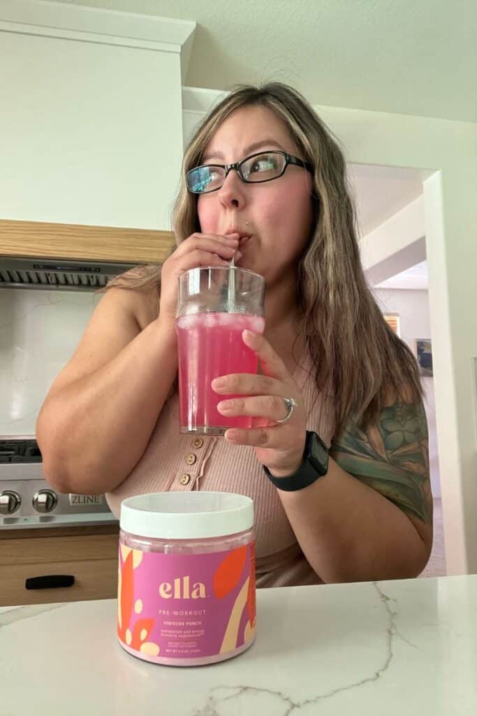image of me (karissa) a brown/blonde drinking ella preworkout out of a glass cup and metal straw