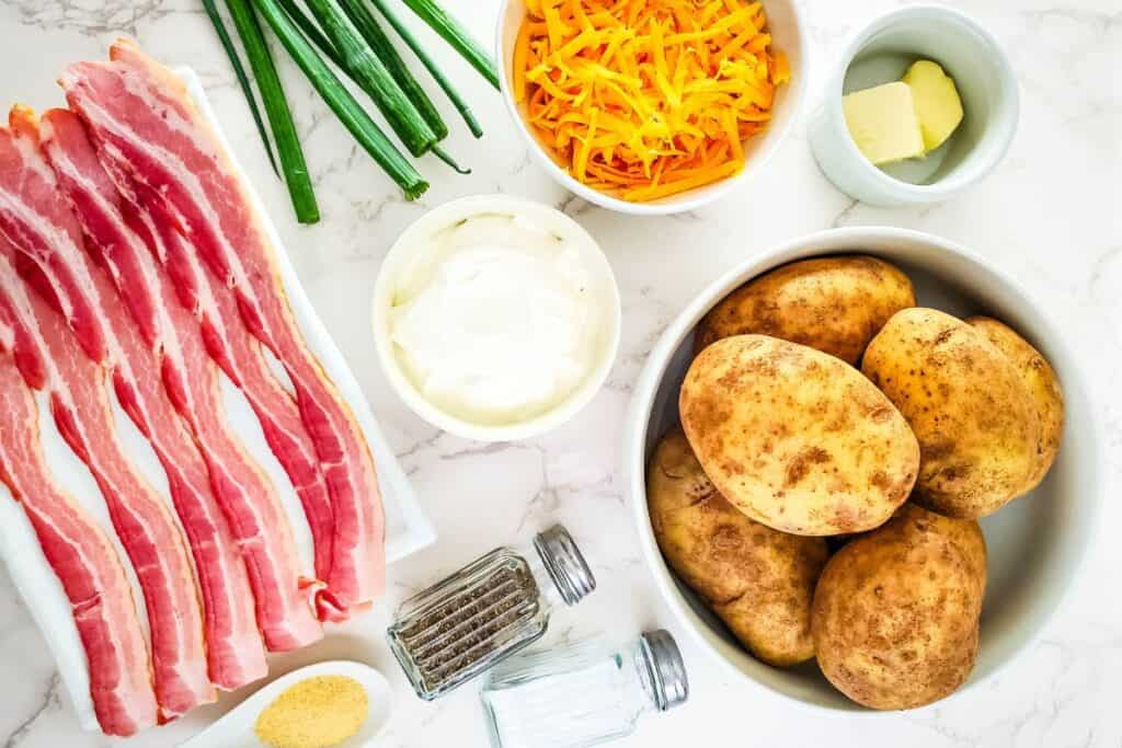 flatlay image of ingredients needed to make twice baked potato casserole (bacon, green onions, salt, pepper, potatoes, cheese, and more)
