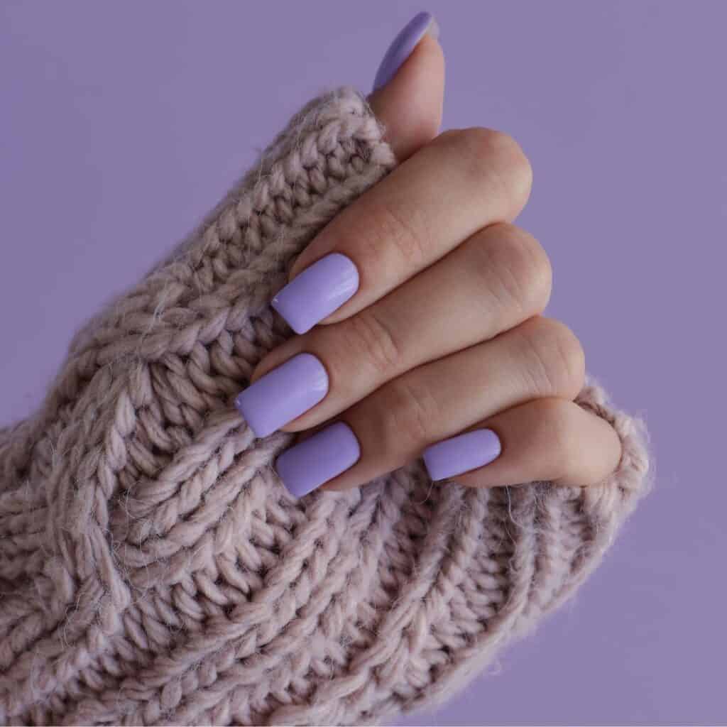 hand with a tan sweater and a lavender purple background and square lavender nails