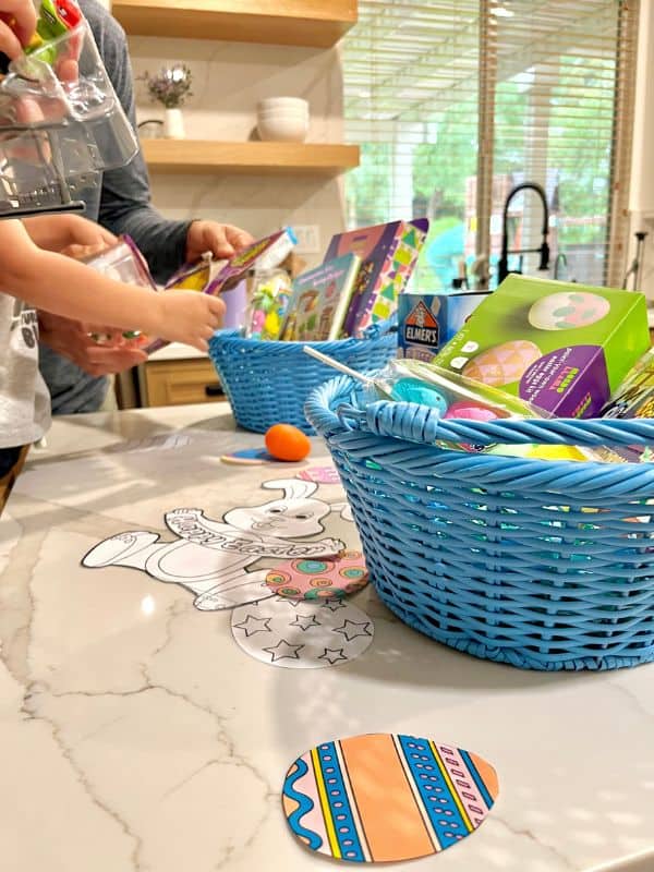 blue easter baskets on a white marble counter filled with shredded paper, crafts, peeps, and other goodies