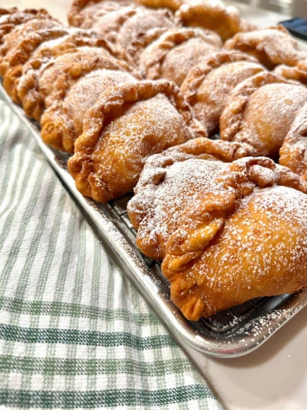 Pasteles de queso on a baking sheet, next to a green and white dish towel
