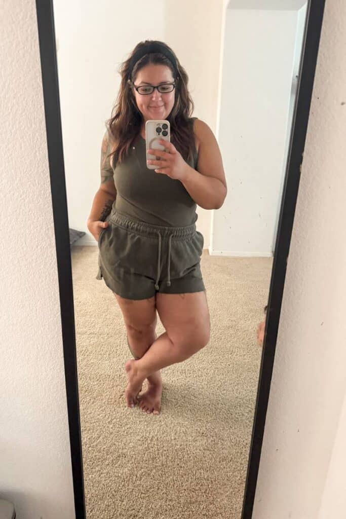 Karissa of Mom After Baby wearing a forest green loungewear tank and shorts set while taking a mirror selfie.