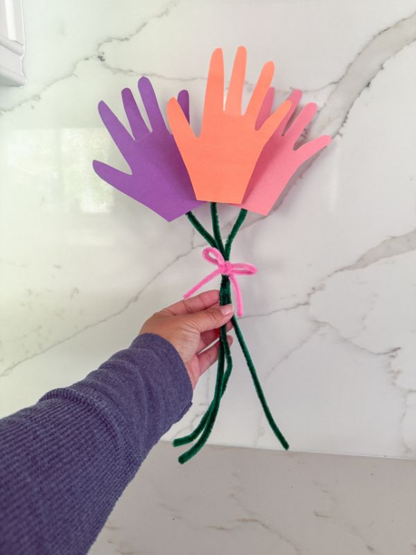 image of a hand holding up a Mother's Day "bouquet" made out of paper handprints and pipe cleaners (a craft for kids)