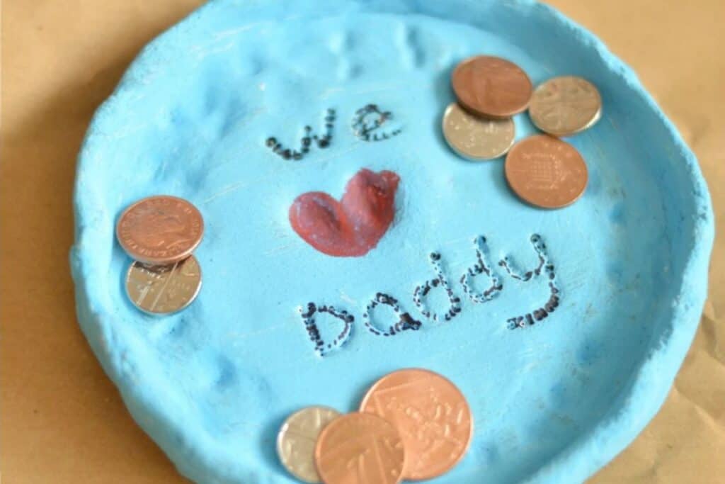 Adorable blue handmade father's day fingerprint dish craft for kids with coins on top of the dish