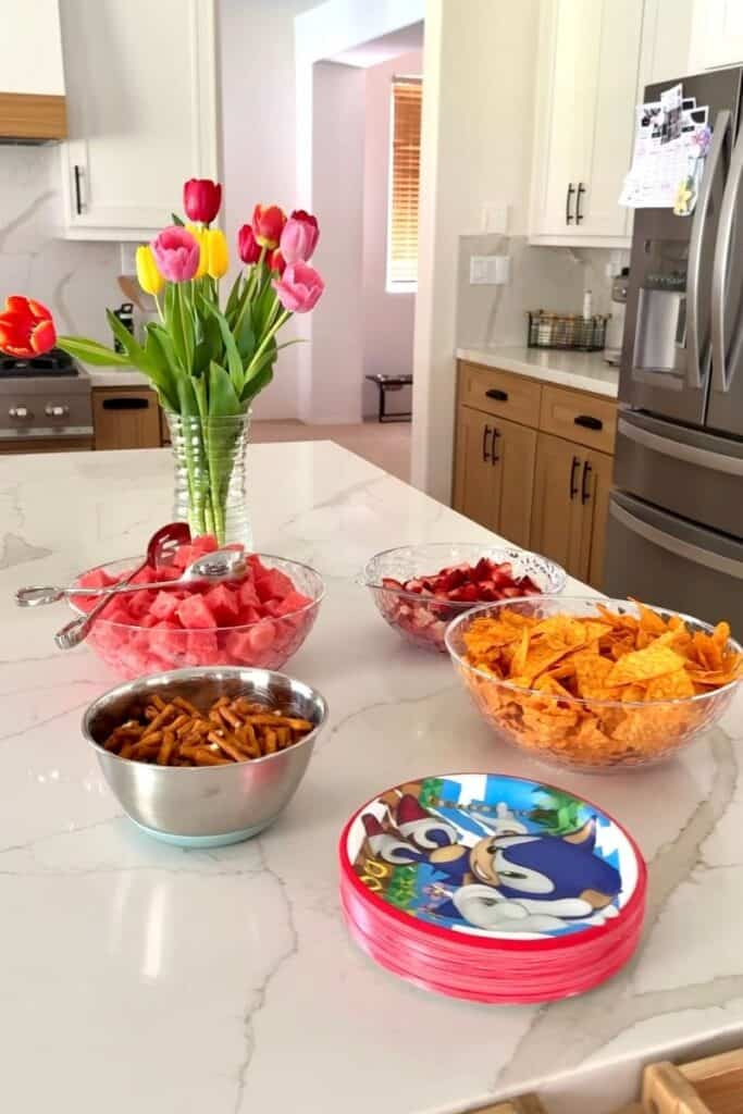Sonic birthday party food ideas - spread of chips and fruit next to some sonic the hedgehog plates on a kitchen island