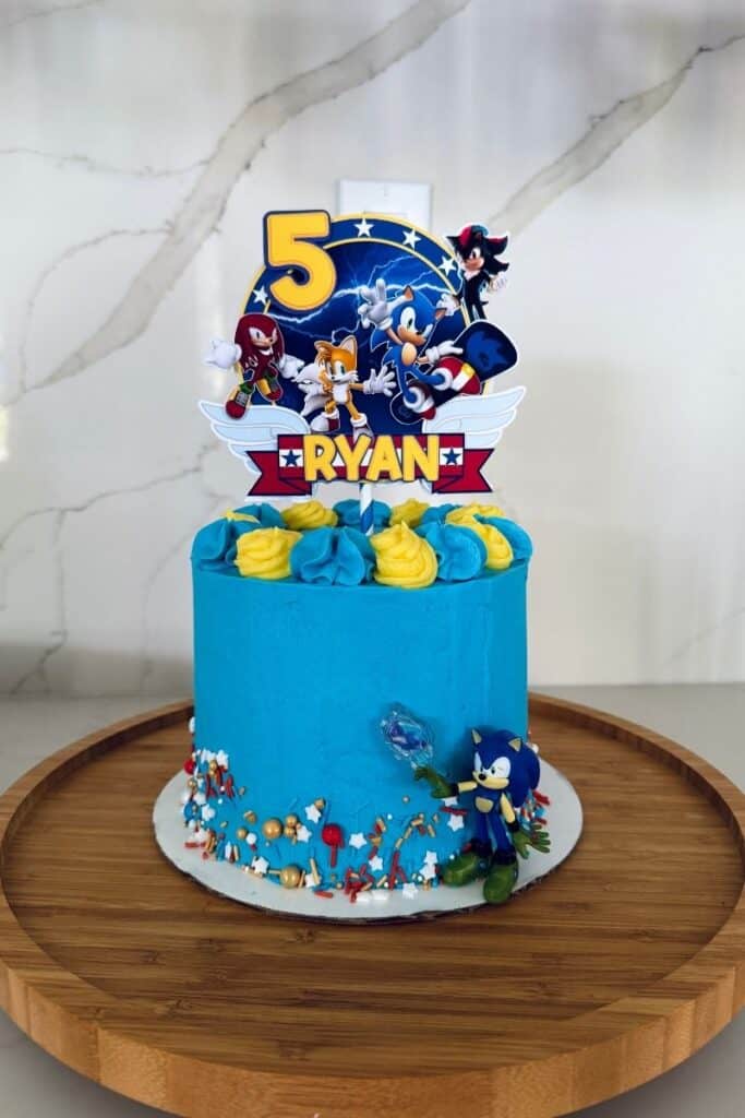 Sonic the Hedgehog DIY Birthday Cake - a blue cake with a sonic cake topper, sprinkles on the side and a sonic toy on the cake.