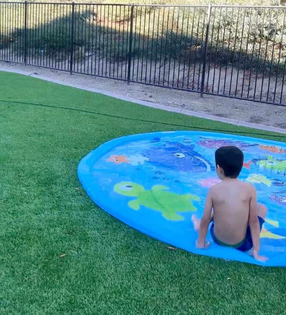 Image of a child sitting in a large splash pad in a yard