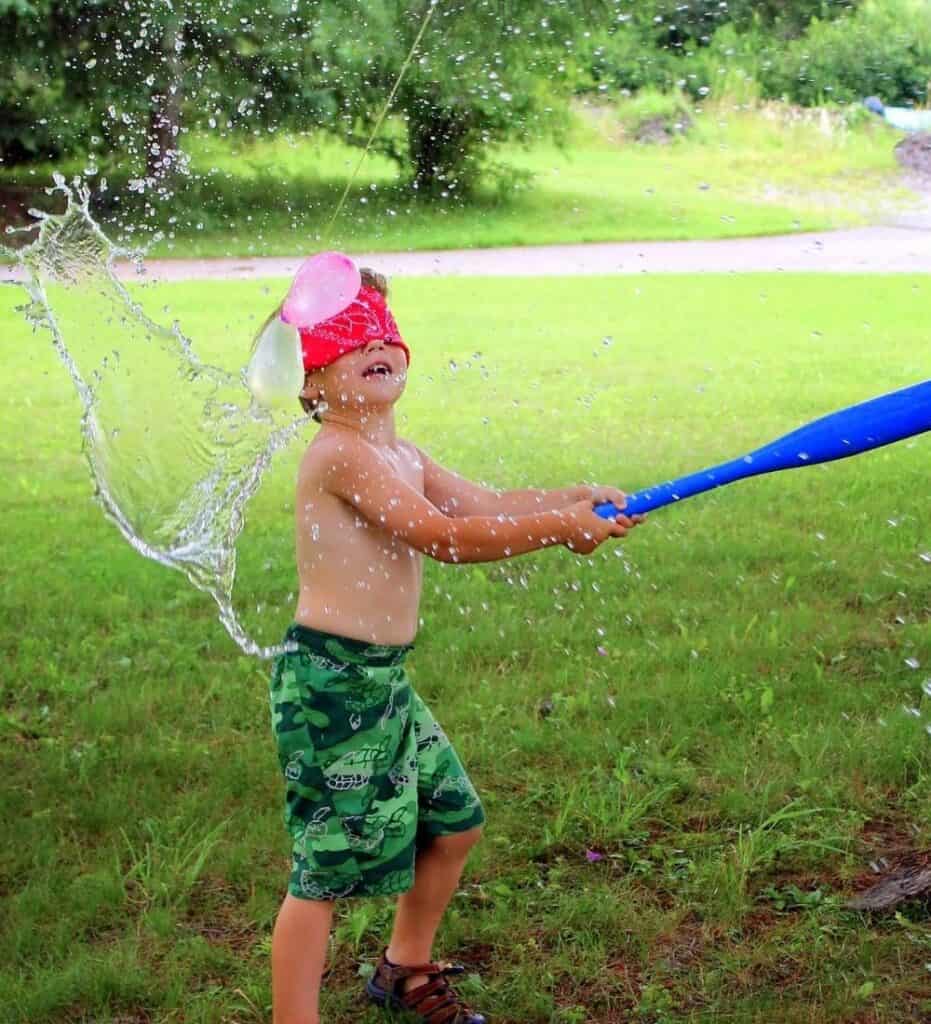 Image of a child blindfolded swinging a bat at a water balloon "pinata"