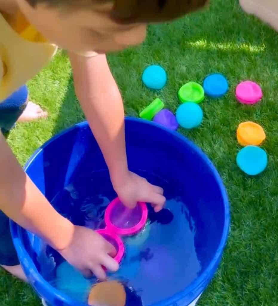 Close up image of child playing with reusable water balloons in a blue bucket full of water